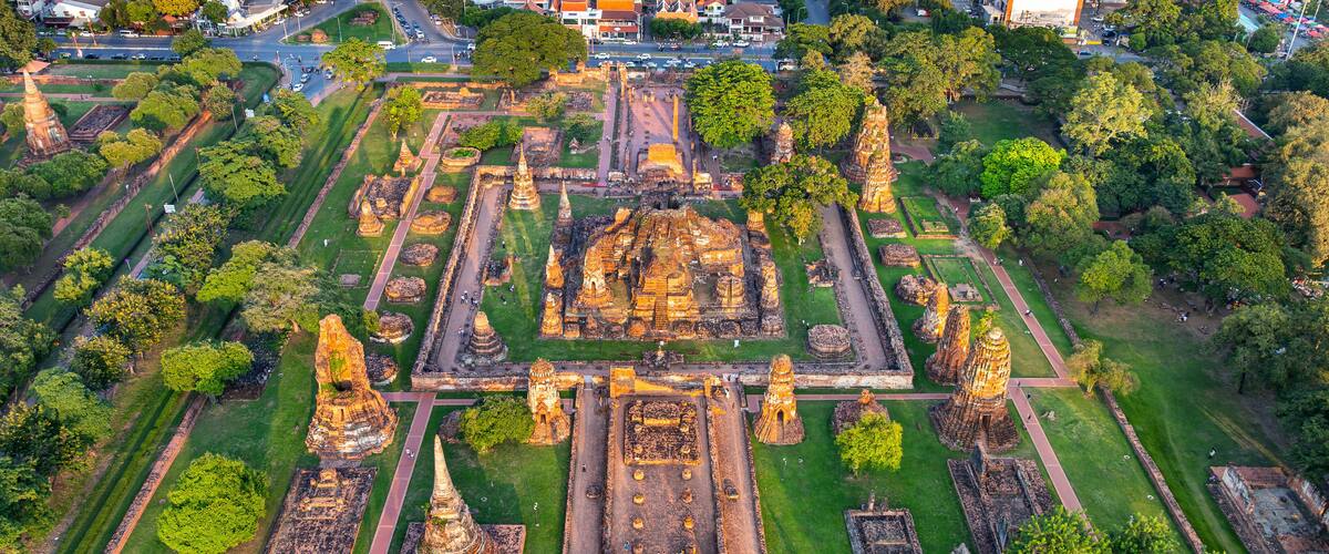 An aerial view of an ancient temple complex with multiple structures, including a central stupa and surrounding smaller buildings, surrounded by well-maintained gardens and pathways.
