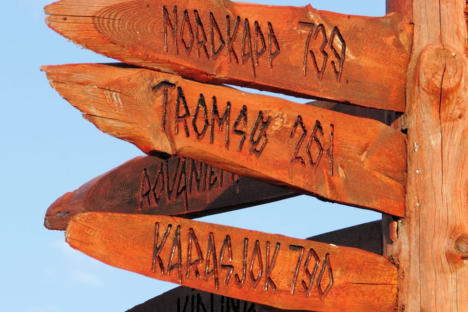 Um sinal de madeira com várias setas indicativas, cada uma com um destino e distância.