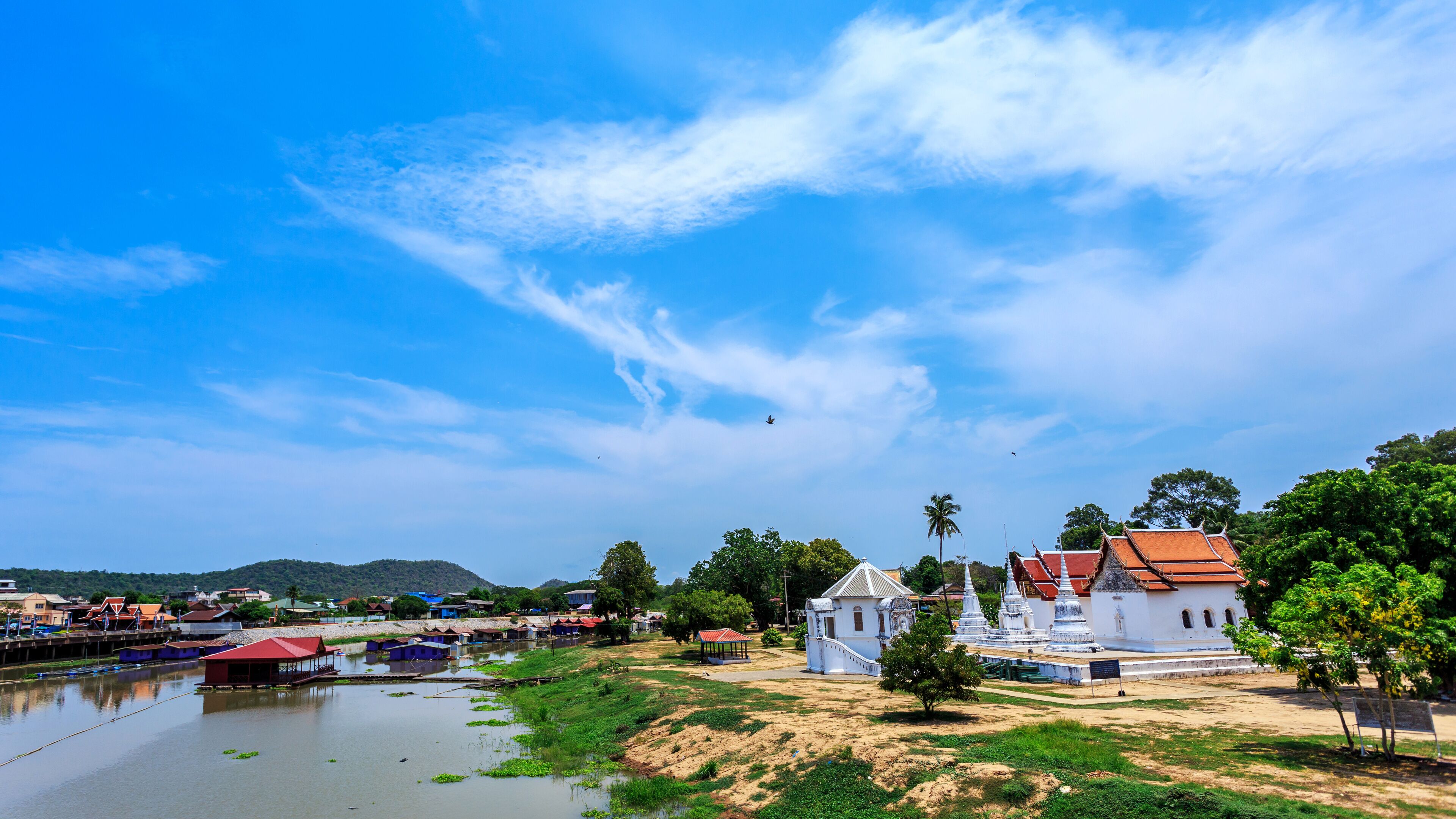 A riverside view with traditional buildings, a temple, and a clear blue sky.