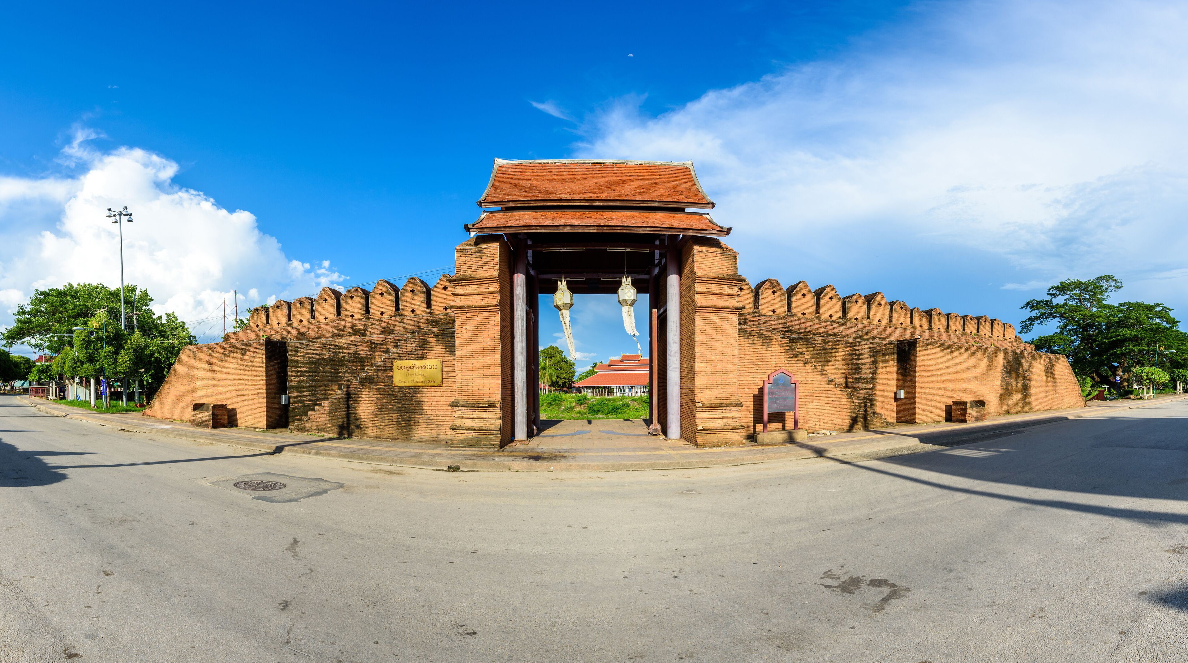 A large brick archway with hanging lanterns, leading to a traditional building with a red roof.