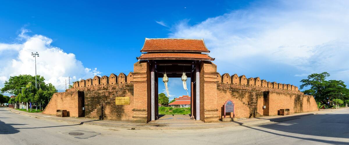 A large brick archway with hanging lanterns, leading to a traditional building with a red roof.