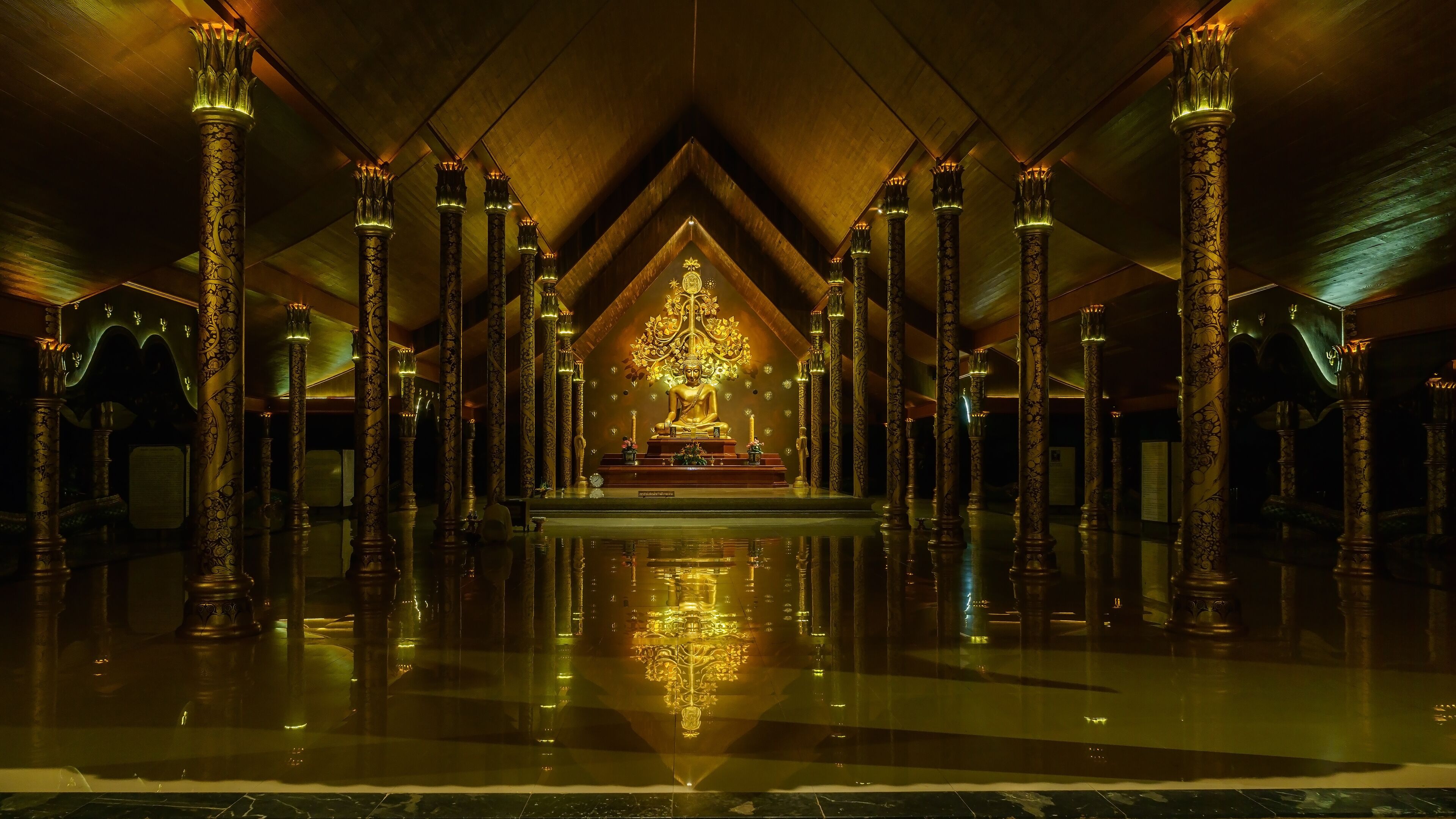 A golden Buddha statue in a temple with ornate pillars and a reflective floor.