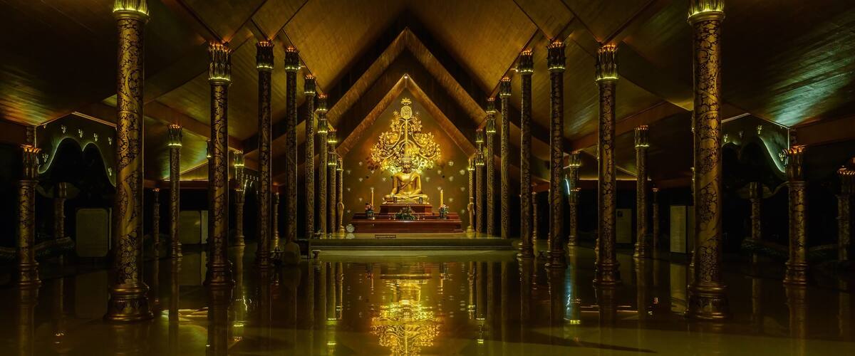 A golden Buddha statue in a temple with ornate pillars and a reflective floor.