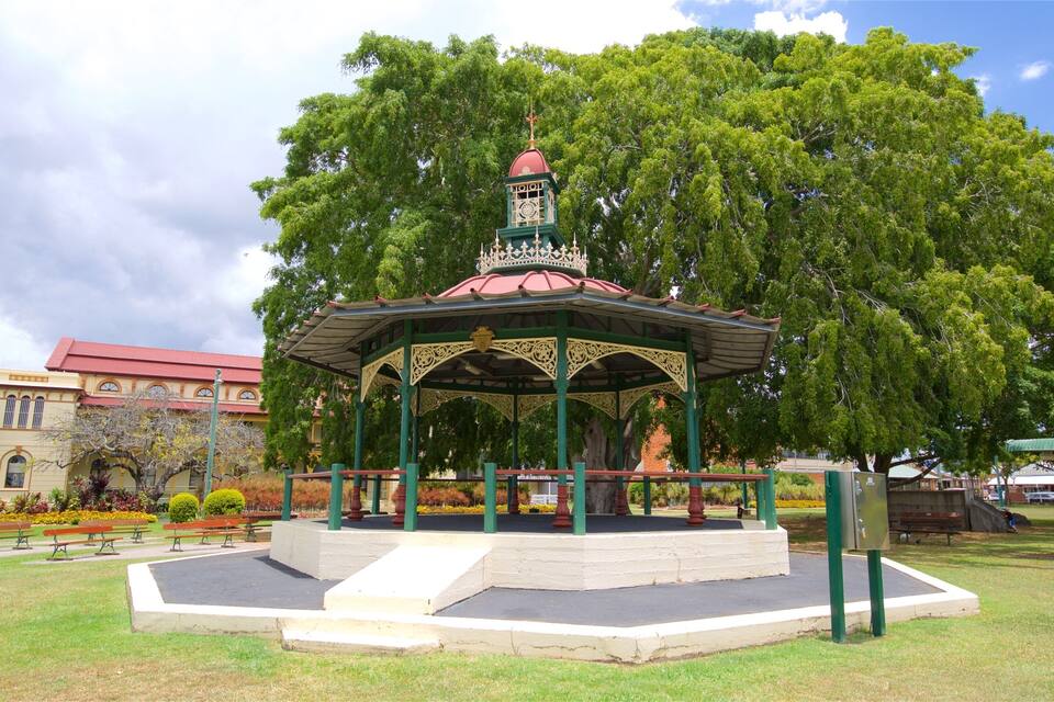 A gazebo with a clock tower in a park with trees and benches.