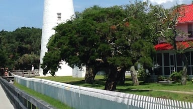 A white lighthouse with a black top, surrounded by trees and a white fence.