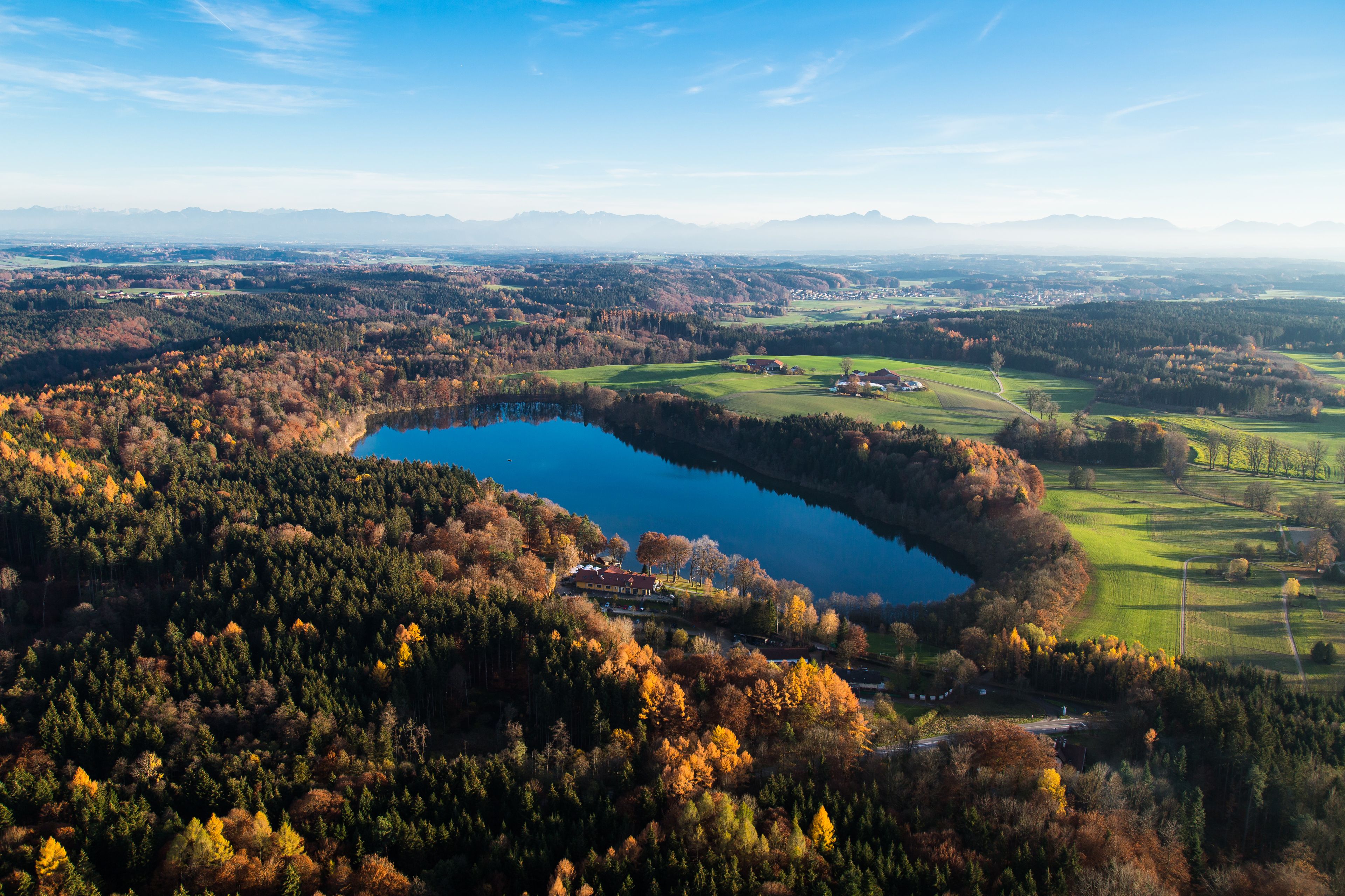A lake surrounded by autumn-colored trees, a small village, and distant mountains.
