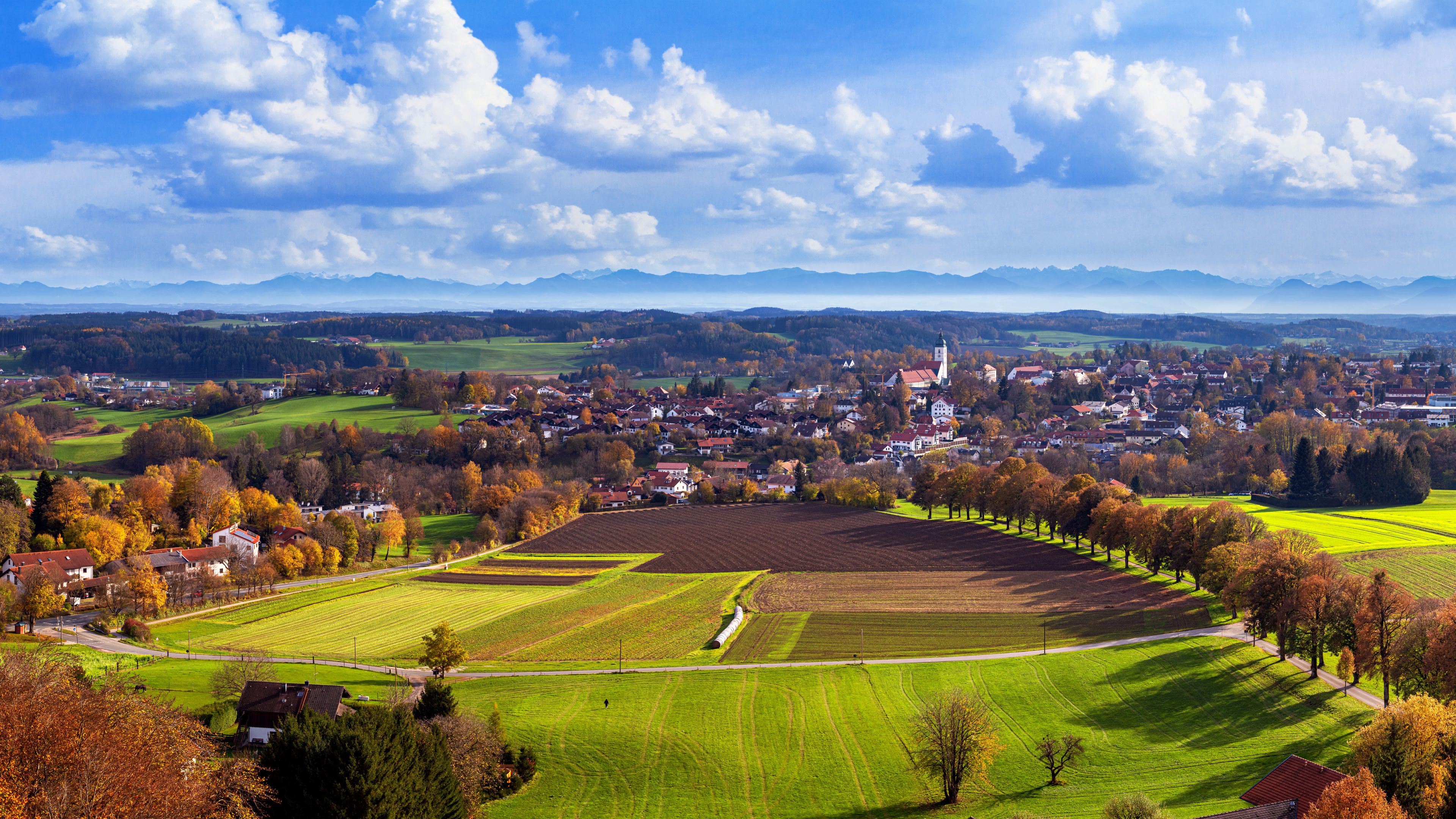 A town with a prominent church, rolling hills, and autumn-colored trees.
