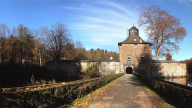 Ein steinerner Turm mit einer Uhr, umgeben von Bäumen und einem Kanal.