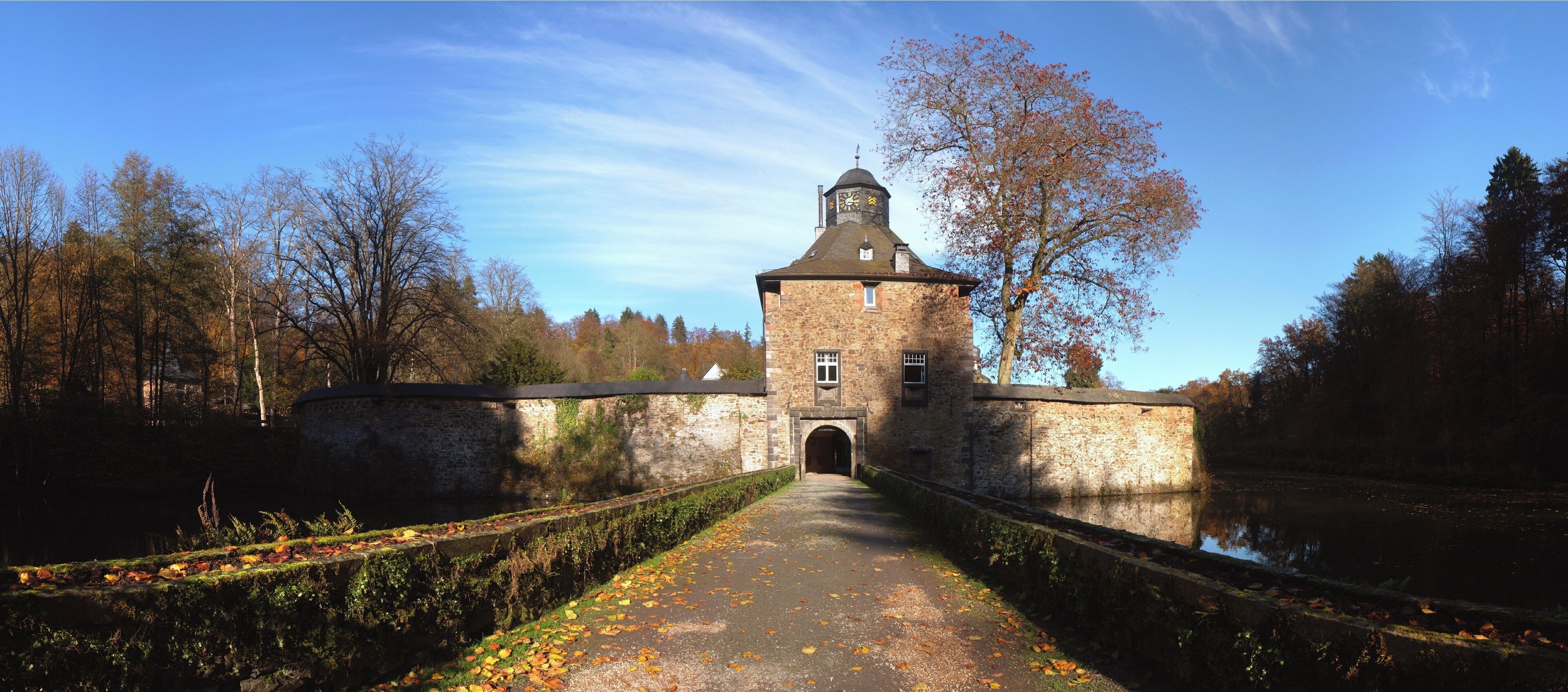 A stone tower with a clock, surrounded by trees and a canal.