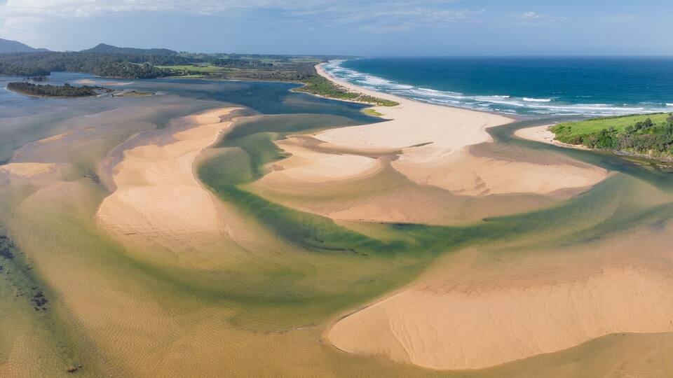 A coastal landscape with sand dunes, a beach, and a clear view of the ocean.