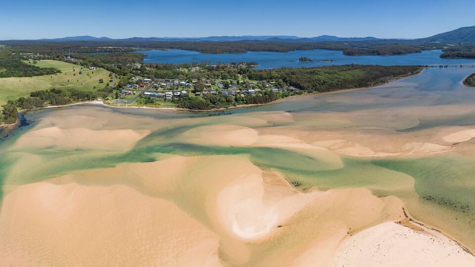 An aerial view of a coastal area with a beach, clear waters, and a residential community.