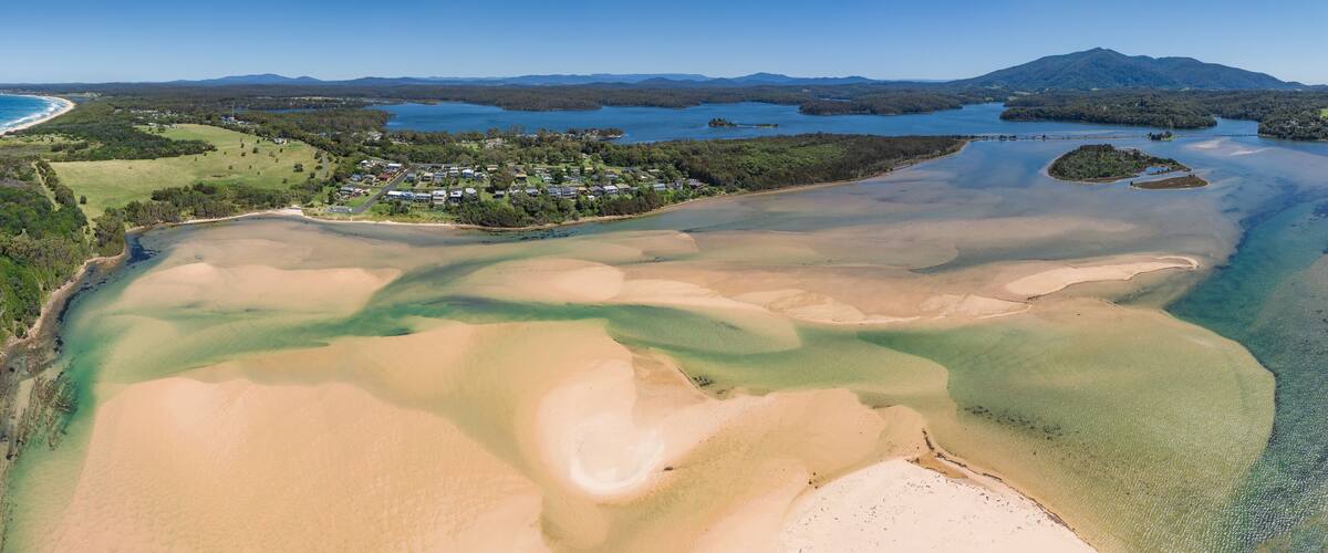 An aerial view of a coastal area with a beach, clear waters, and a residential community.