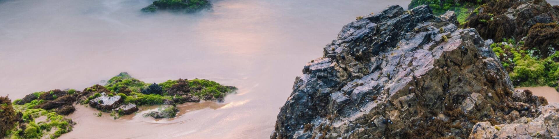 A coastal landscape with rocky formations and calm waters during sunset.