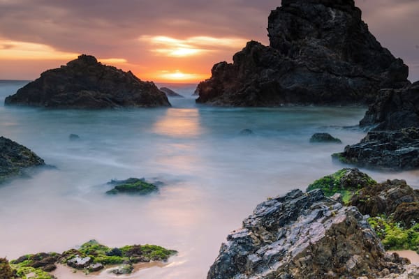 A coastal landscape with rocky formations and calm waters during sunset.
