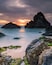 A coastal landscape with rocky formations and calm waters during sunset.