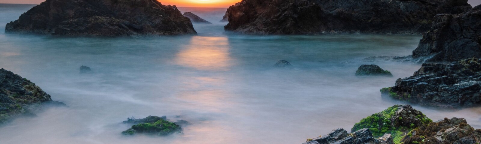 Paisaje costero con formaciones rocosas y aguas tranquilas al atardecer.