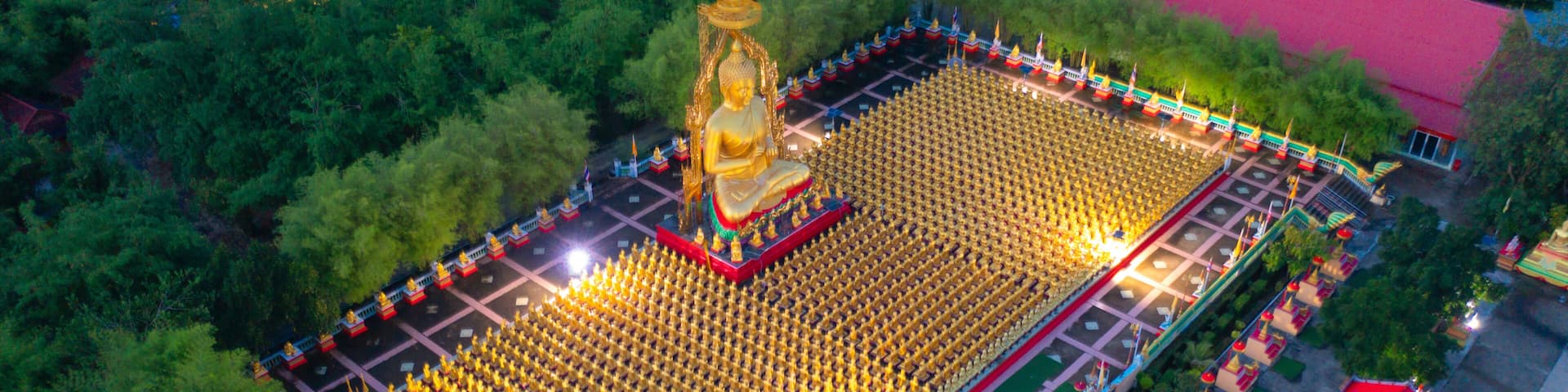 An aerial view of a temple complex with a large golden statue, a red-roofed building, and a surrounding garden.