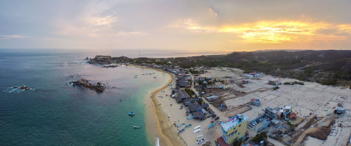 A coastal town with a beach, boats, and a fort on a hill.