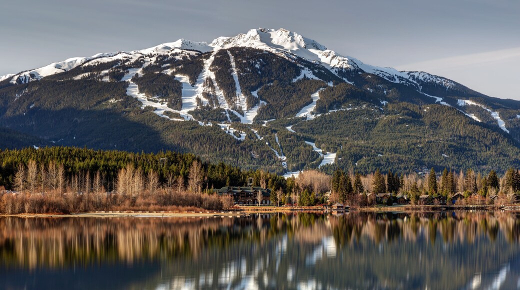 Une montagne aux sommets enneigés, un lac paisible et une zone boisée parsemée de bâtiments.