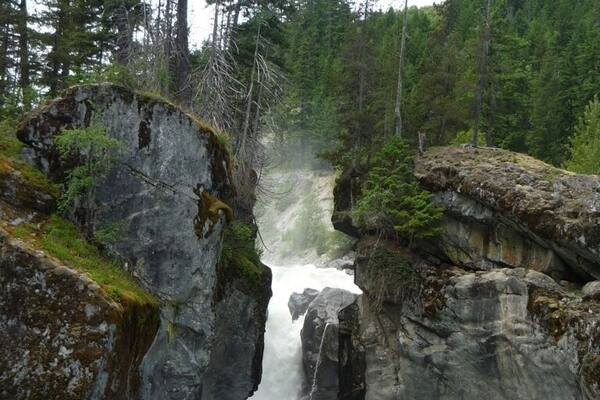 Ein Wasserfall stürzt durch eine felsige Schlucht, umgeben von dichtem Wald.