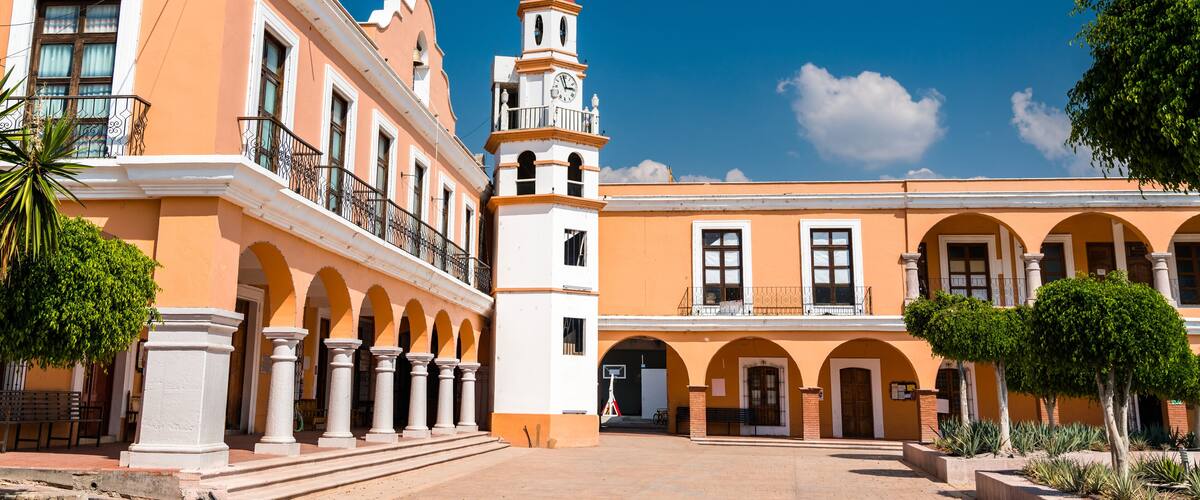 A historic building with a clock tower, arched walkways, and a clear blue sky.