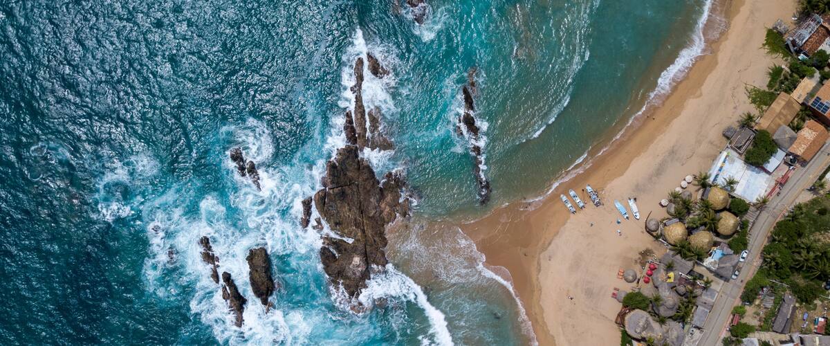 An aerial view of a beach with rocky outcrops and a row of houses along the shore.