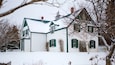 A snow-covered house with green shutters and a white facade.