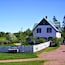 A white house with a green roof, surrounded by a white picket fence and lush greenery.