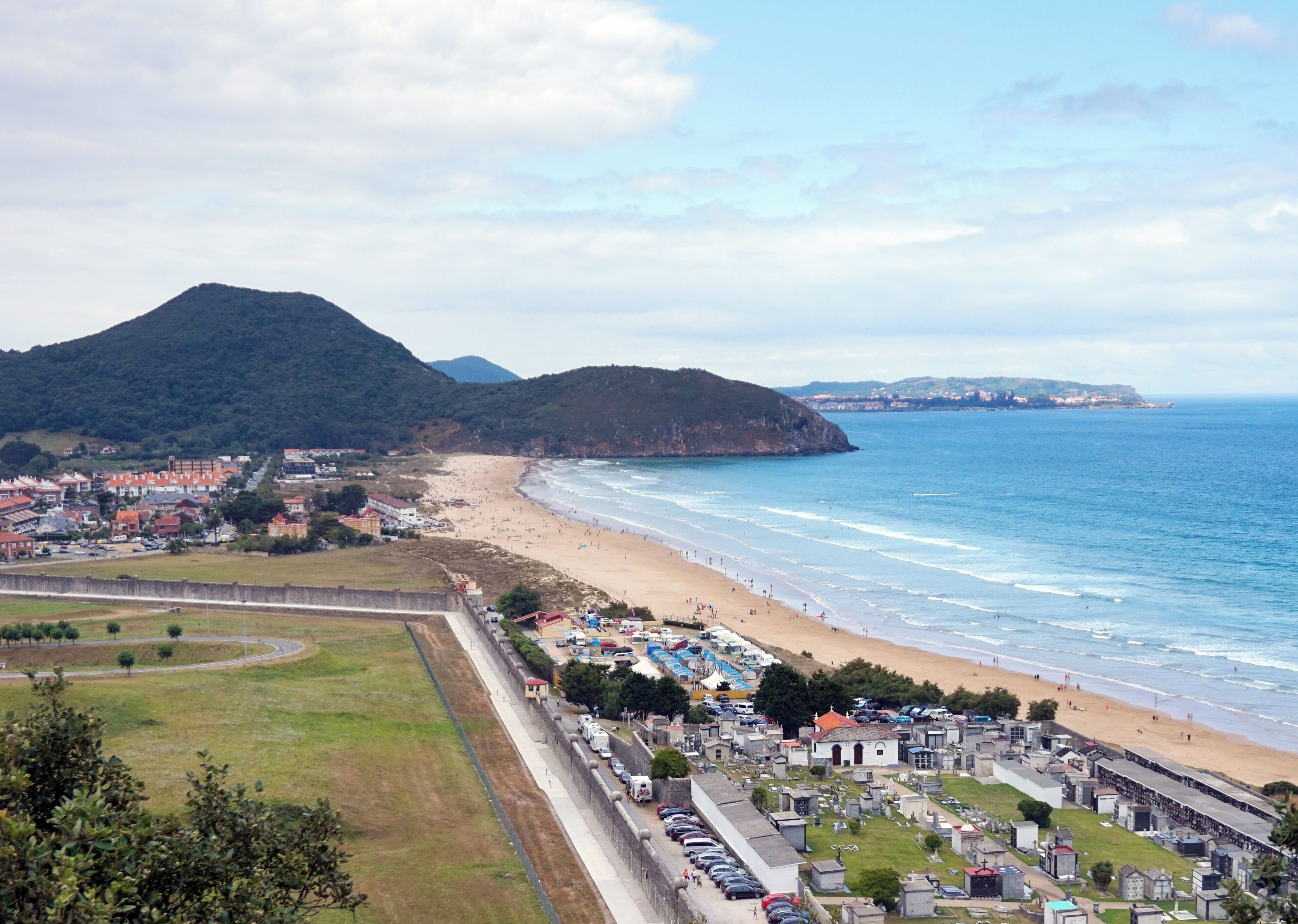 A coastal town with a beach, a cemetery, and a mountain in the background.