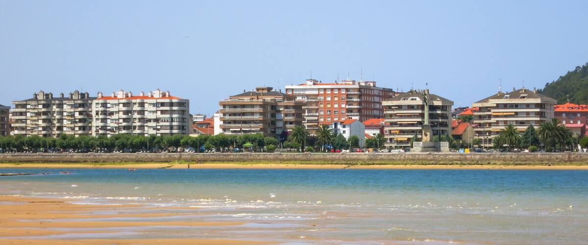 A beach with clear water and buildings in the background.