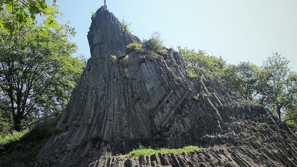A large rock formation with a cross on top, surrounded by trees.