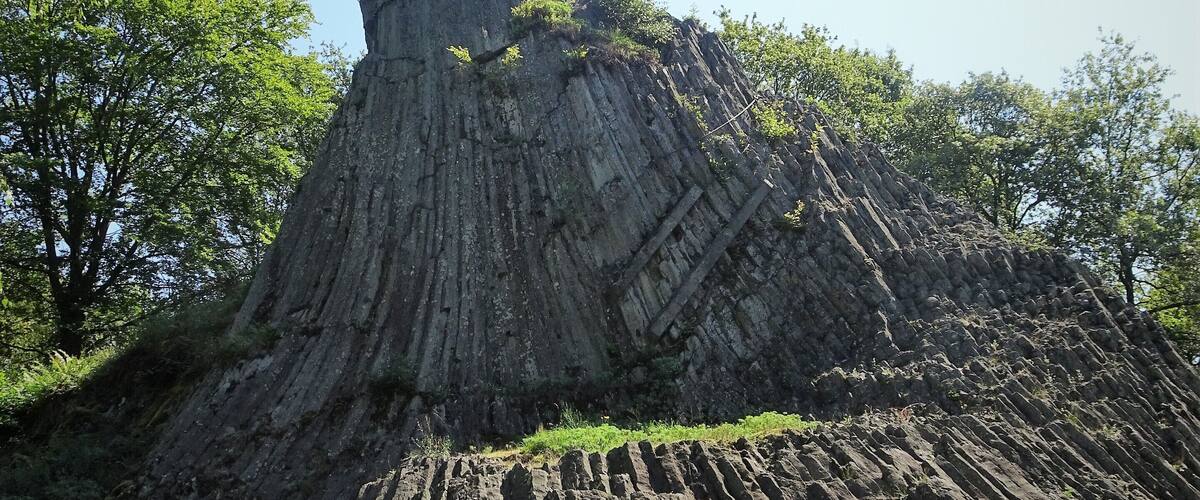 A large rock formation with a cross on top, surrounded by trees.