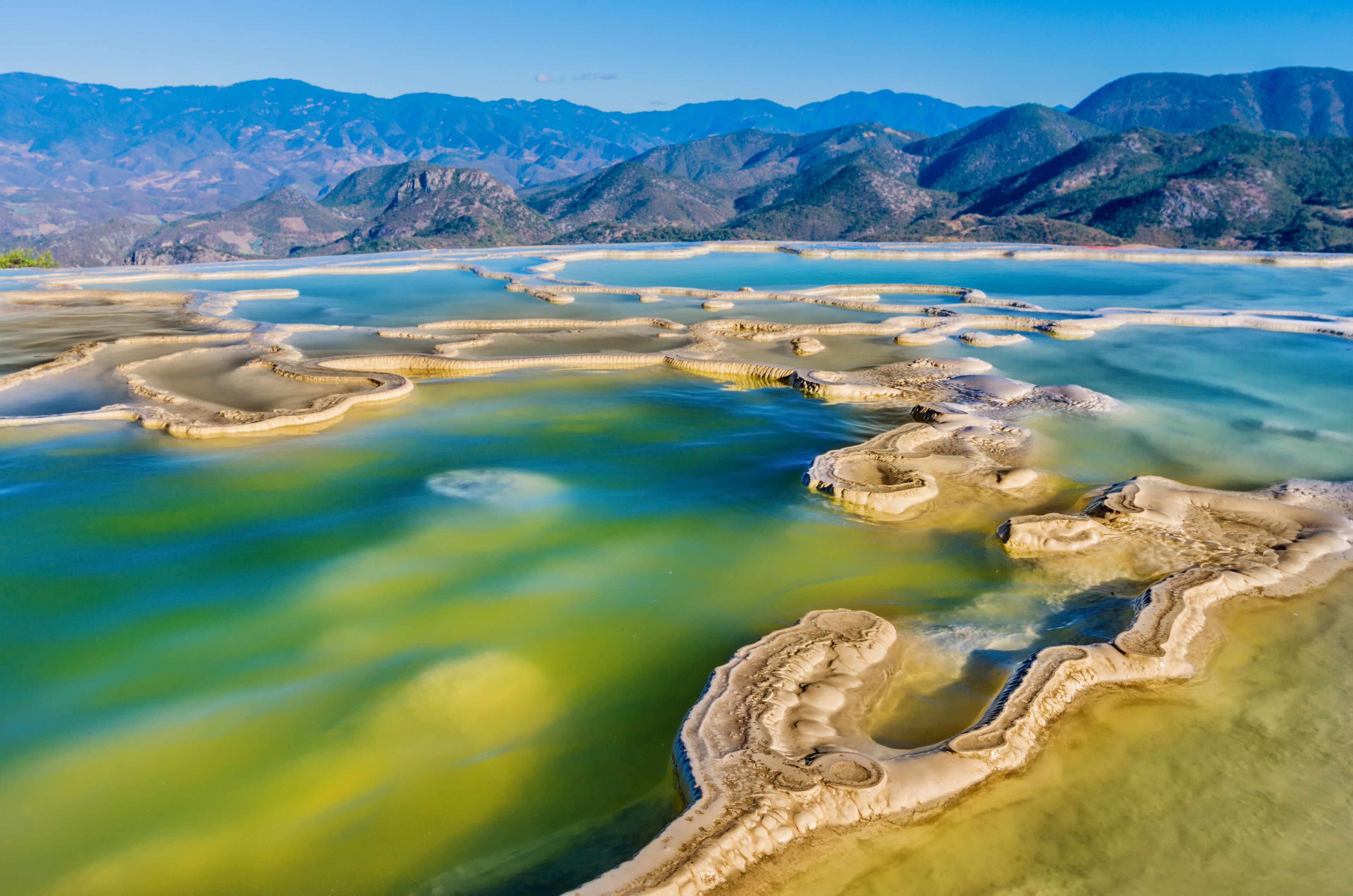 A panoramic view of terraced mineral pools with mountains in the background.