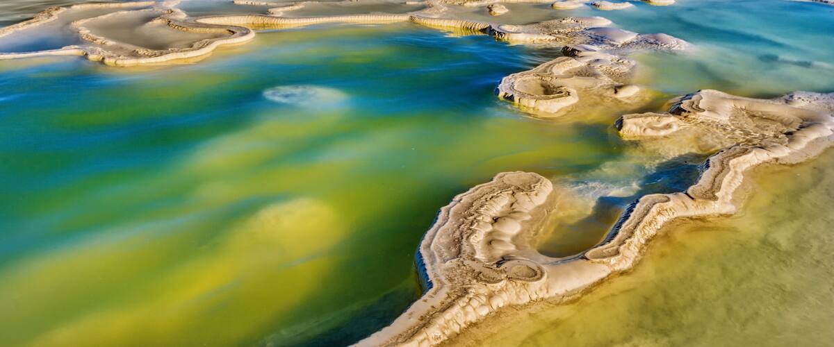 A panoramic view of terraced mineral pools with mountains in the background.