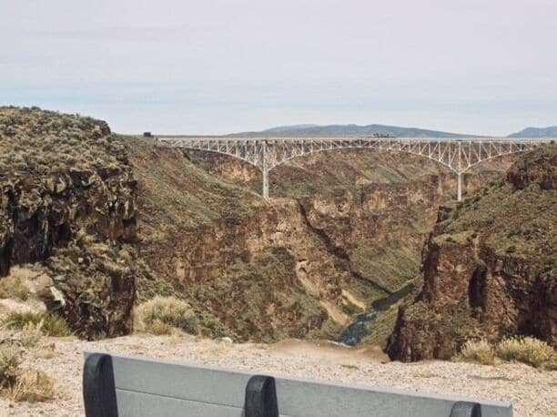 A bridge over a canyon with rocky terrain and sparse vegetation.