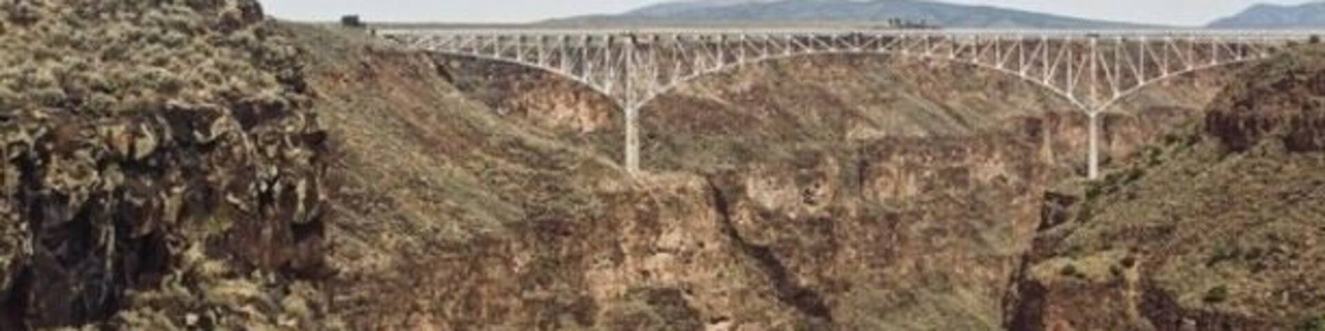 A bridge over a canyon with rocky terrain and sparse vegetation.