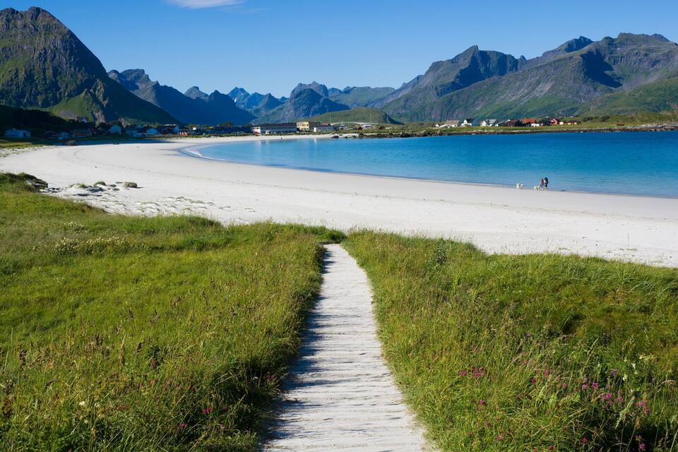 A coastal path leading to a beach with mountains in the background.