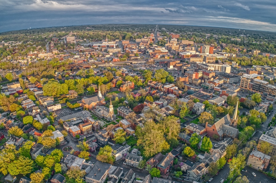 An aerial view of a city with a mix of historic and modern buildings, surrounded by green spaces and trees.