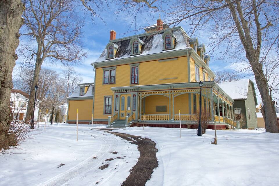 A yellow Victorian-style house with a porch and a snow-covered yard.