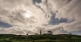 A lighthouse, a white house, and a hill with a grassy landscape.
