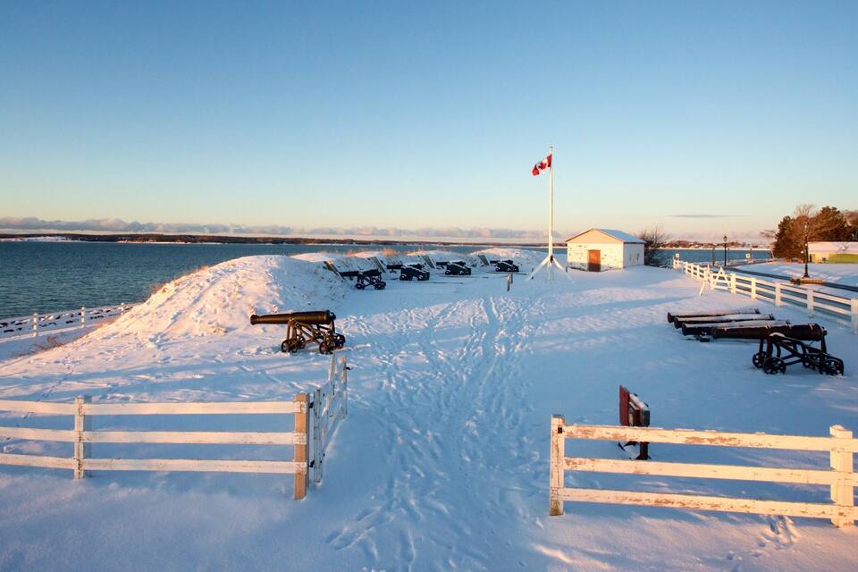 A snow-covered pier with cannons and a flagpole, overlooking a calm body of water.