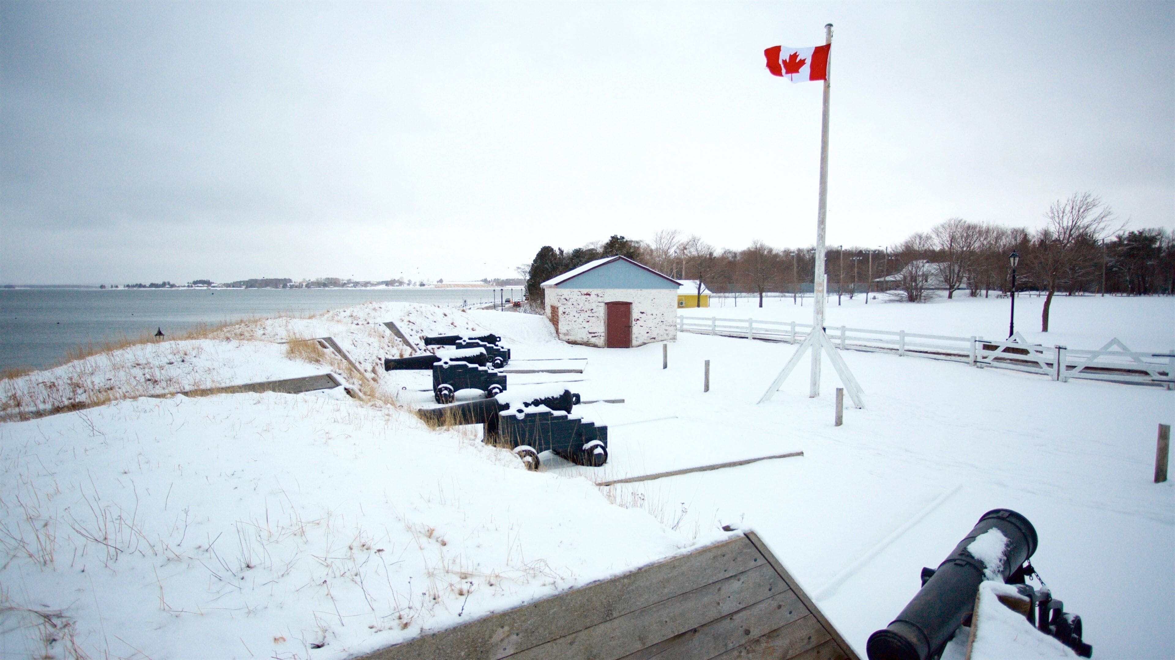 A snow-covered pier with a Canadian flag, a small shed, and a row of parked vehicles.