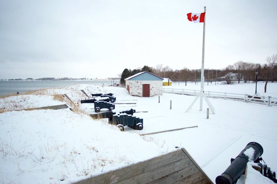 A snow-covered pier with a Canadian flag, a small shed, and a row of parked vehicles.