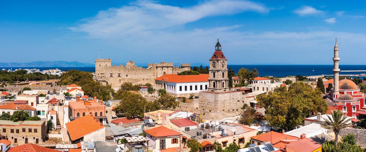 A coastal cityscape with historic architecture, including a castle, a church, and a mosque with domes.