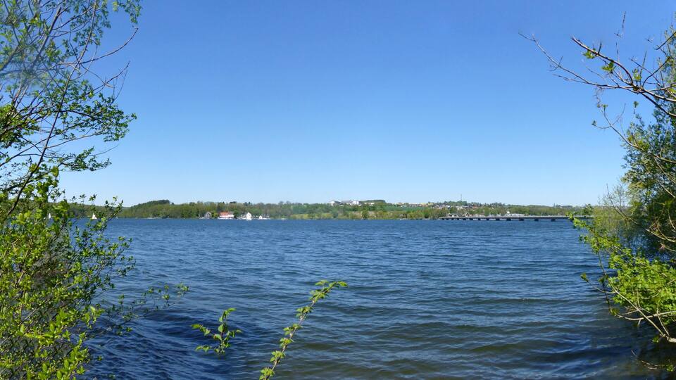 A calm lake with boats, surrounded by trees and a distant shoreline with buildings.