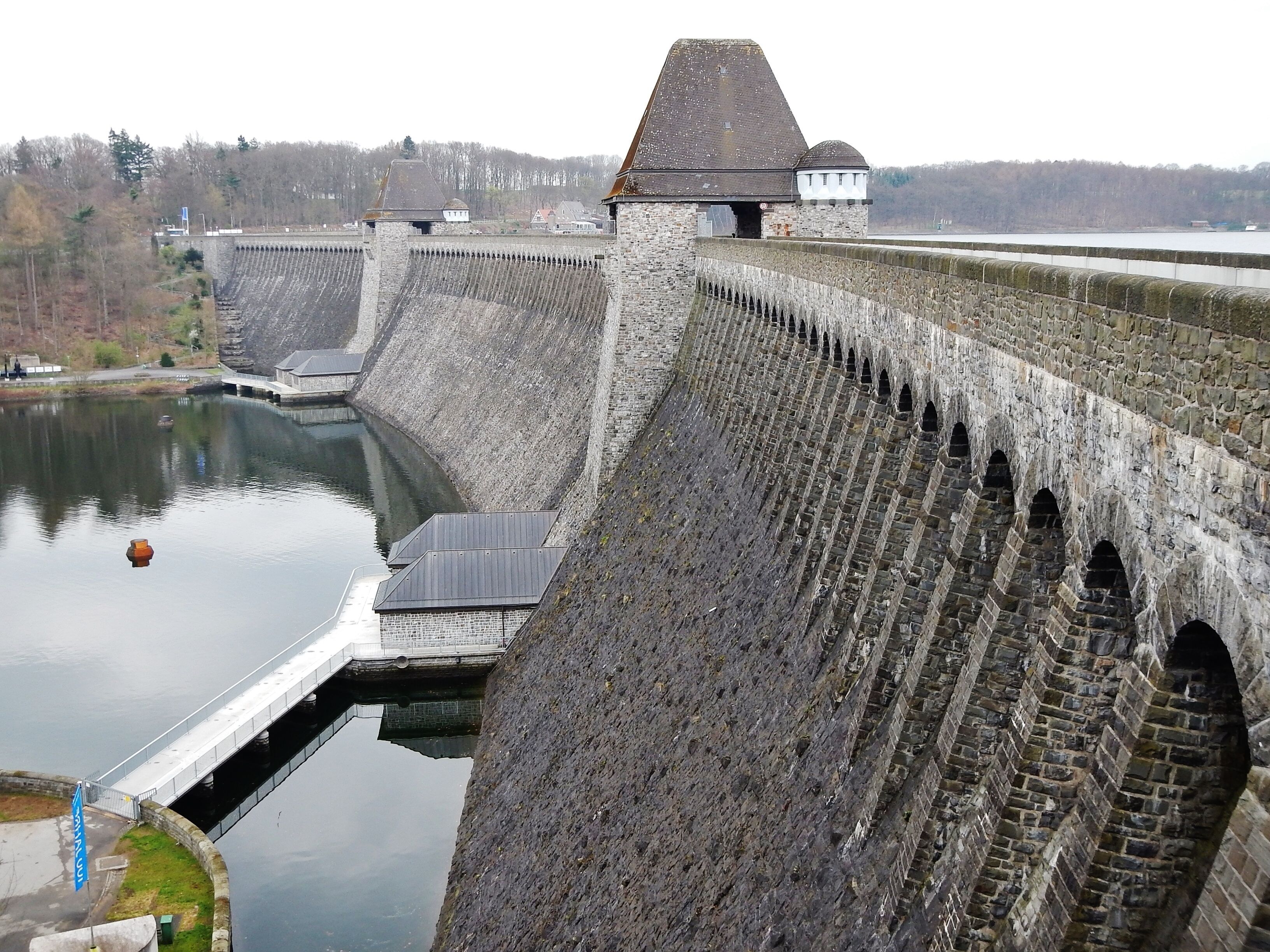 A large dam with multiple gates, a small building, and a calm river.