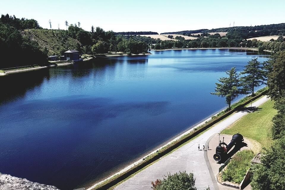 A calm lake surrounded by greenery and a paved walkway.