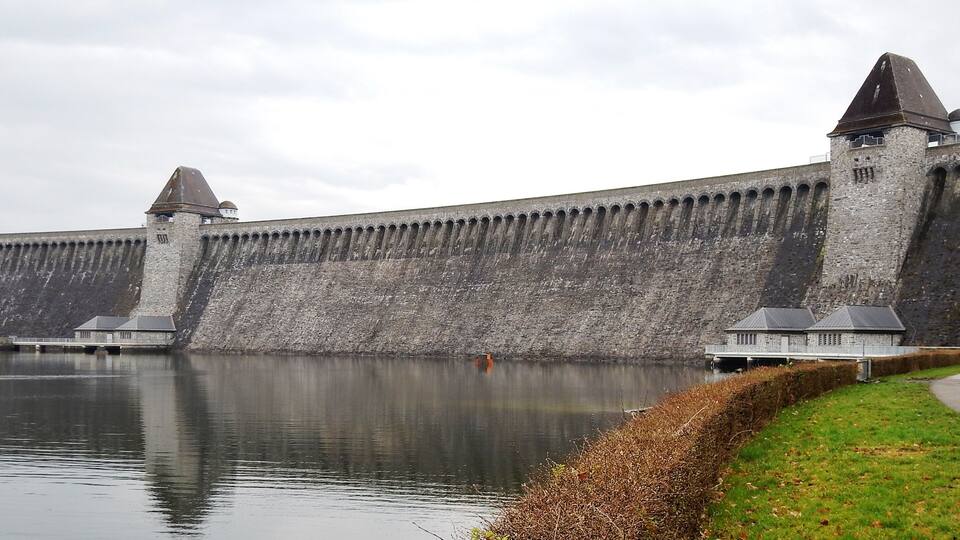 A large stone wall with towers and a calm body of water in the foreground.