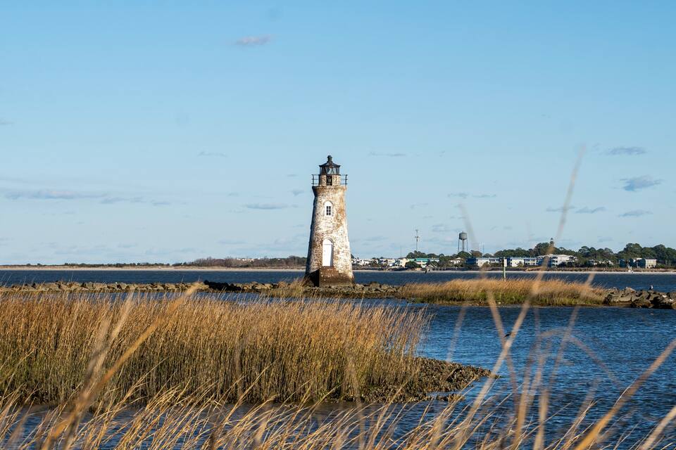 A lighthouse by a body of water with tall grasses in the foreground.