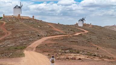 Woman heading down a dirt road towards the white stone windmills in a town in Ciudad Real (Spain)